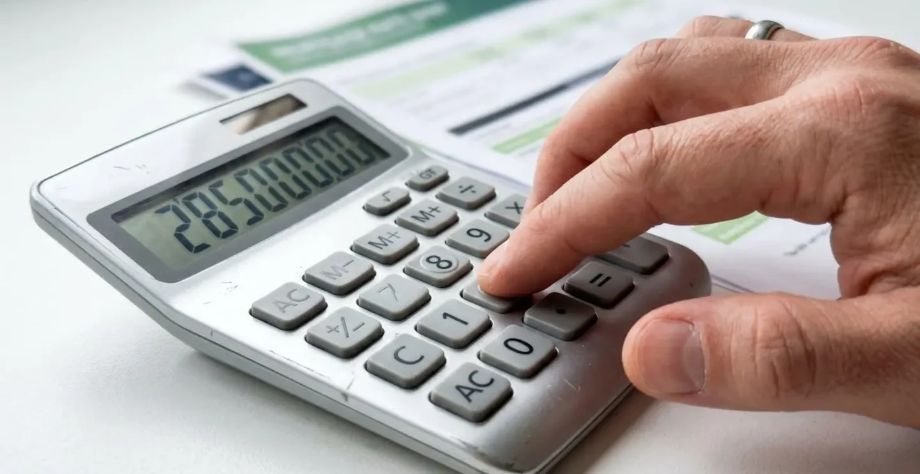 Gros plan sur une main utilisant une calculatrice moderne posée à côté d'une feuille de taux de crédit immobilier, avec un arrière-plan flouté
